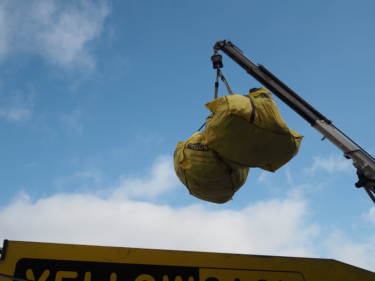 The crane arm lifting a full 3,000 lb Yellowsack off a driveway