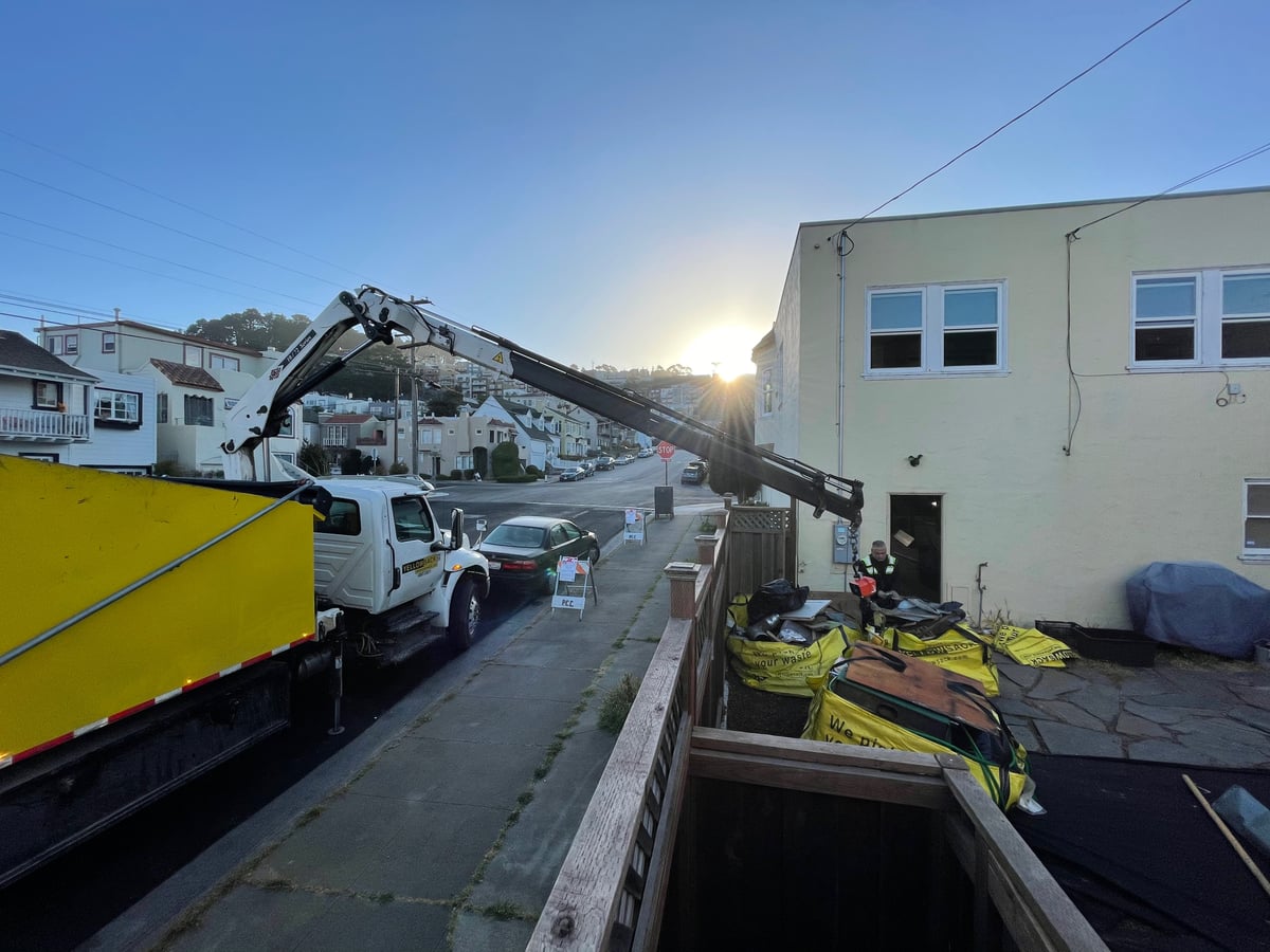 A crane truck lifting a full bag over a fence, showing the 20 ft reach
