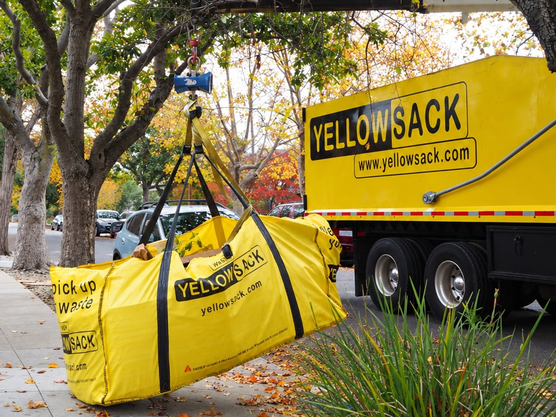 A Yellowsack crane truck lifting a full dumpster bag off a driveway