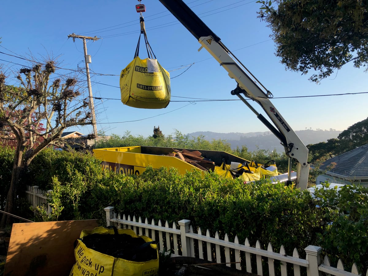 The crane arm lifting a full Yellowsack over a fence